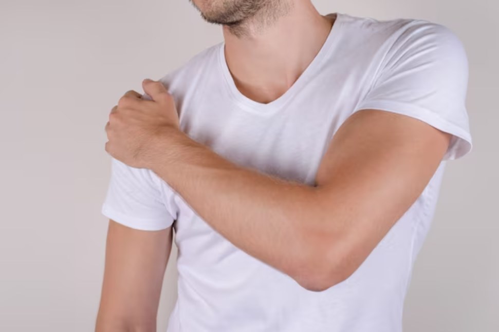 a man touching his shoulder on an isolated grey background