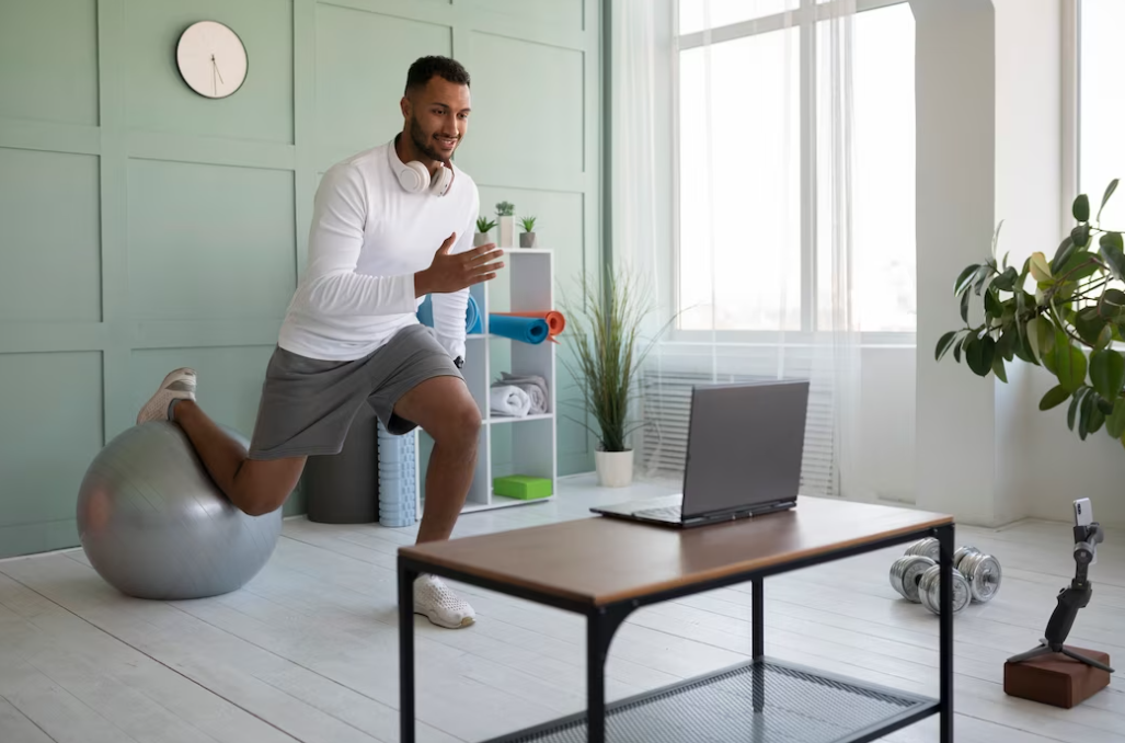 man training with a gym ball and watching on the laptop on the table in front of him