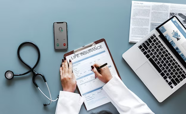 A doctor fills out an insurance policy, medical equipment, a phone and a laptop are nearby