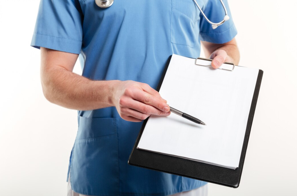 man in a blue medical t-shirt with a stethoscope holds a sheet and pen on it