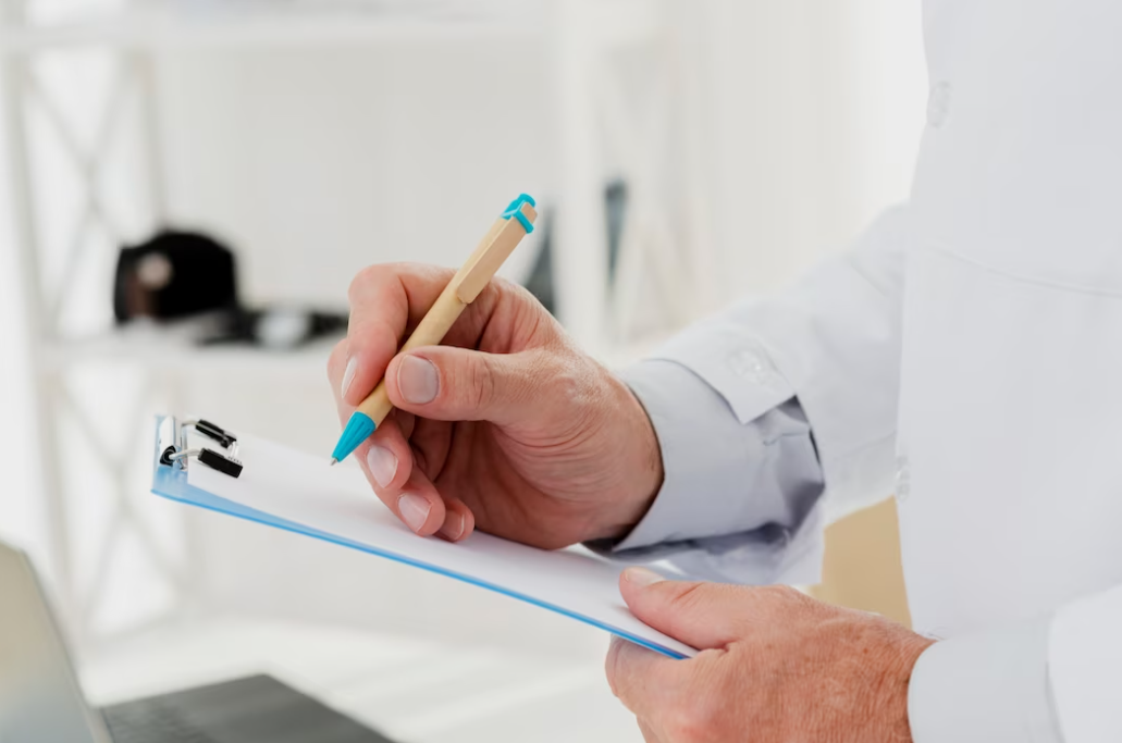 a side view of a man in white medical clothing holding a sheet and making notes with a pen