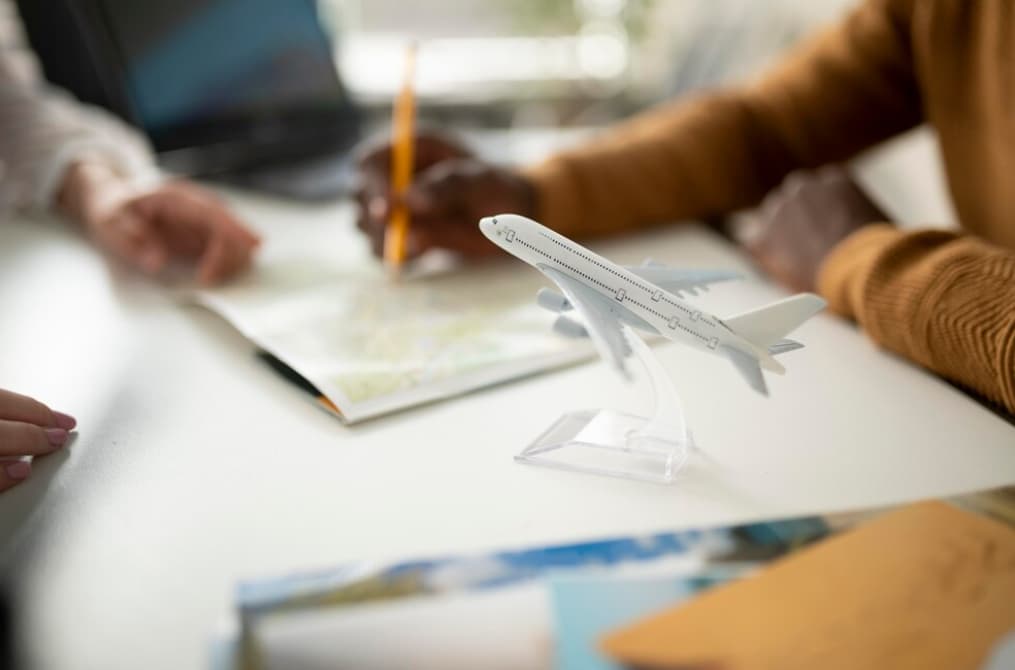 Close-up of hands planning a trip with a map, pencil, and model airplane on the table.