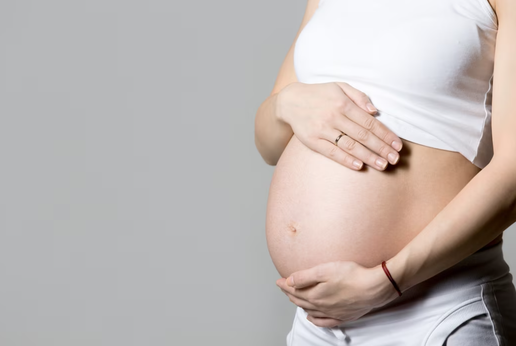 pregnant woman in white short t-shirt holds her belly with two hands